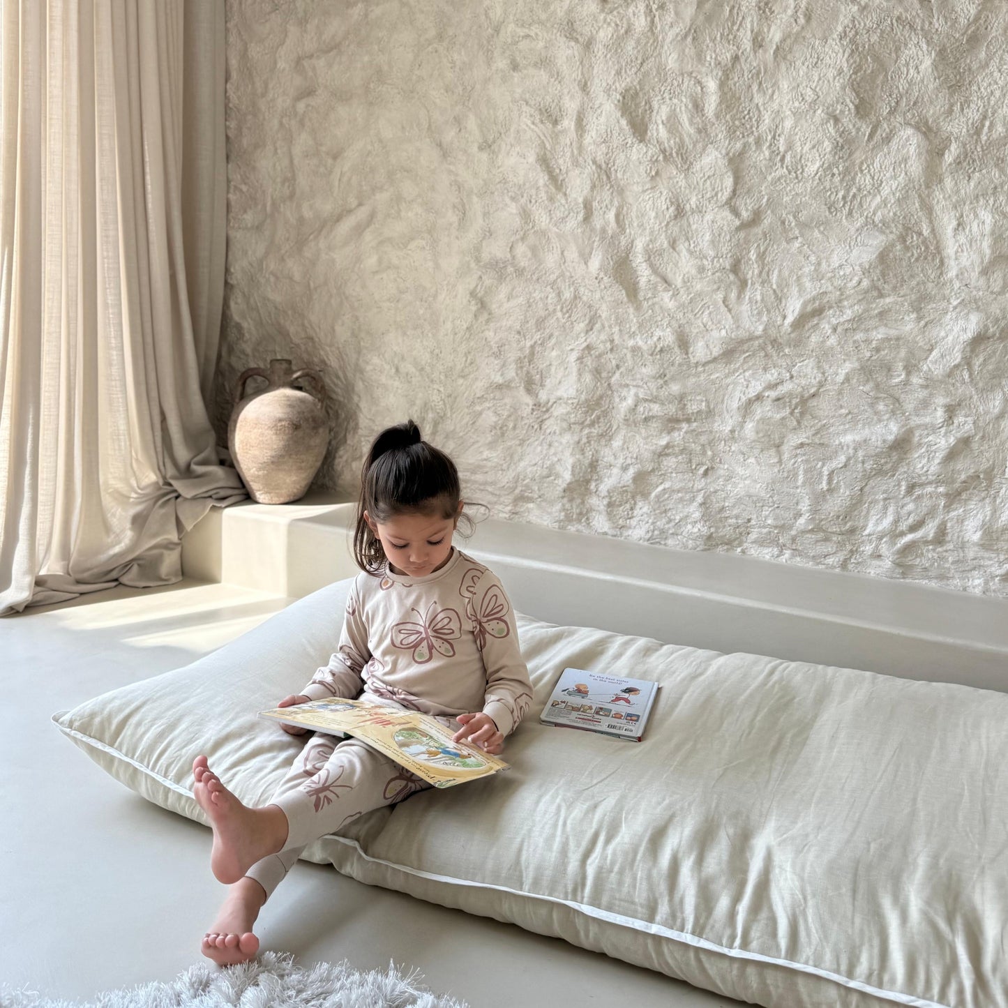 Child reading a book on a never far home roll up bed in a softly lit room with textured walls.