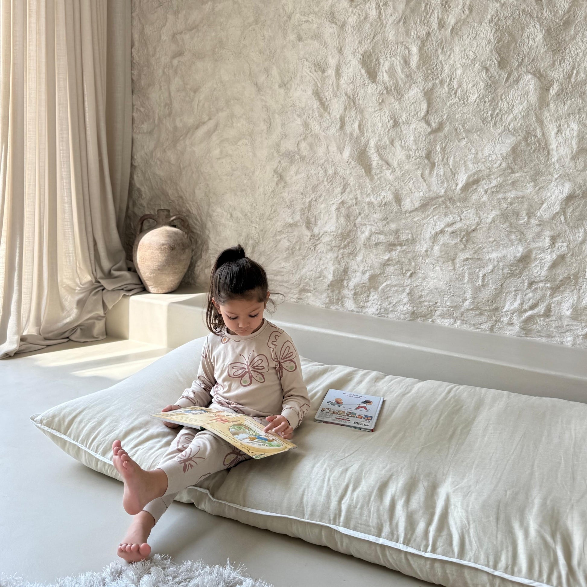 Child reading a book on a never far home roll up bed in a softly lit room with textured walls.