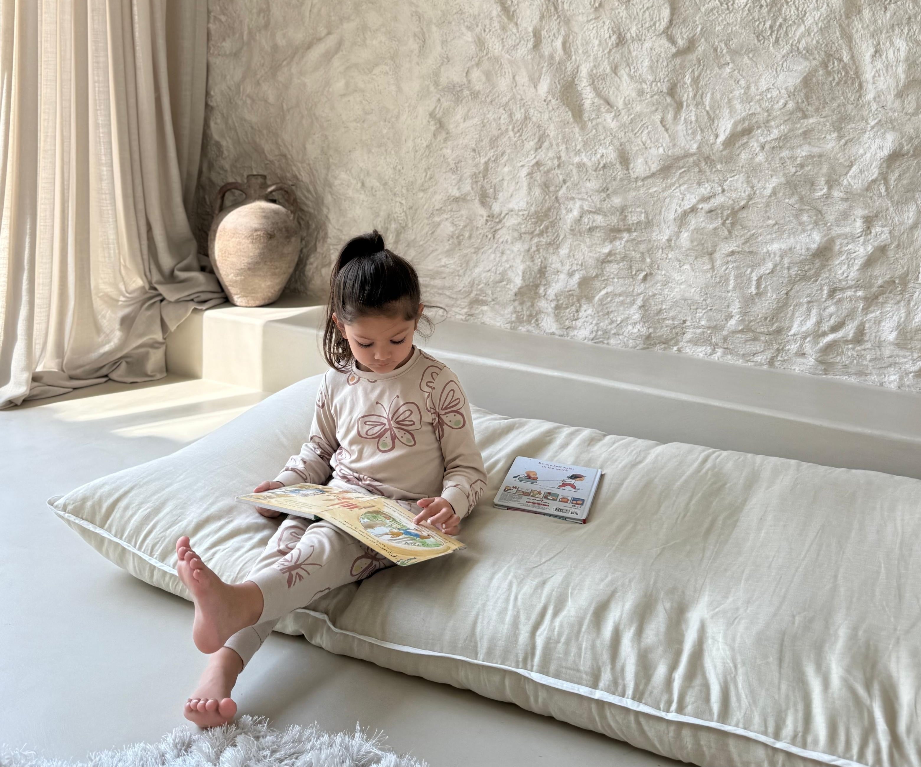 Child reading a book on a never far home roll up bed in a softly lit room with textured walls.