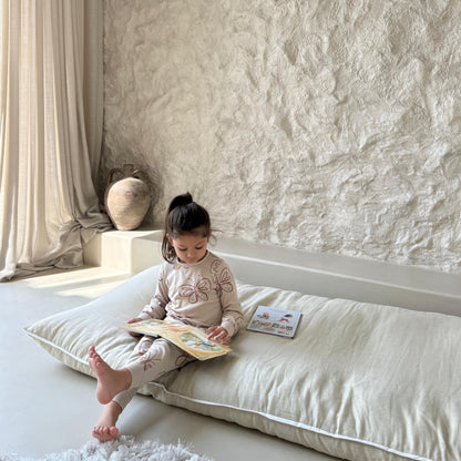 Child reading a book on a never far home roll up bed in a softly lit room with textured walls.