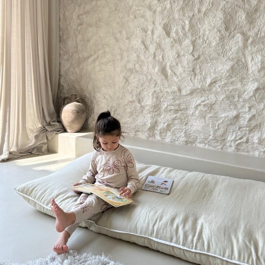 Child reading a book on a never far home roll up bed in a softly lit room with textured walls.